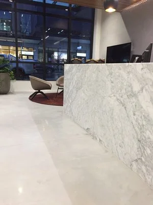 Modern office reception area with a marble desk, two chairs, and large windows overlooking a city street.