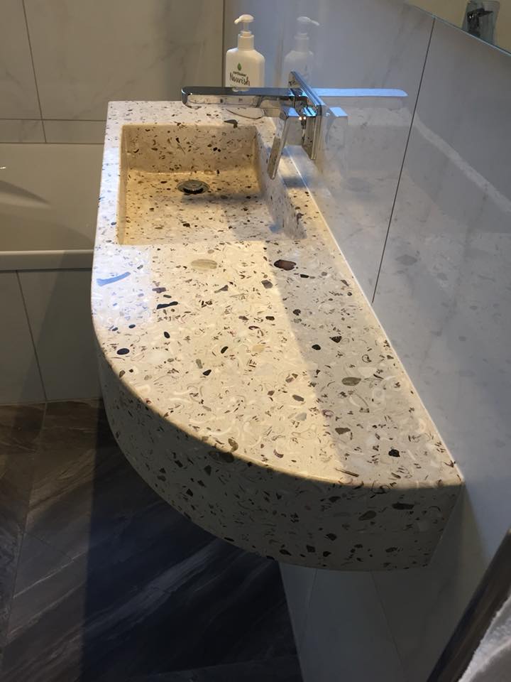 Bathroom with terrazzo sink, wall-mounted faucet, and a bottle of hand soap on the counter.