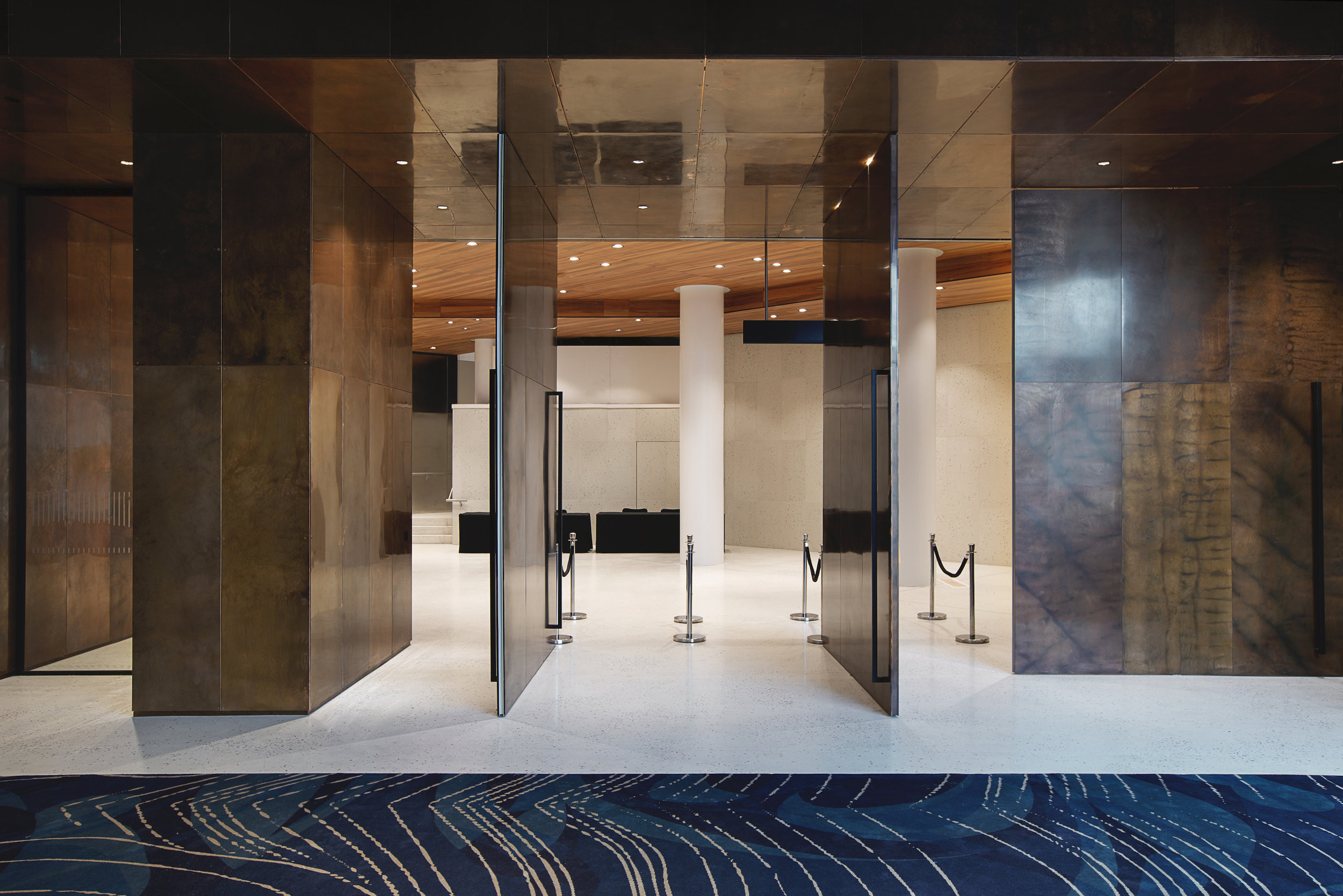 Entrance to a modern lobby with metallic walls, white pillars, and a dark blue patterned carpet.