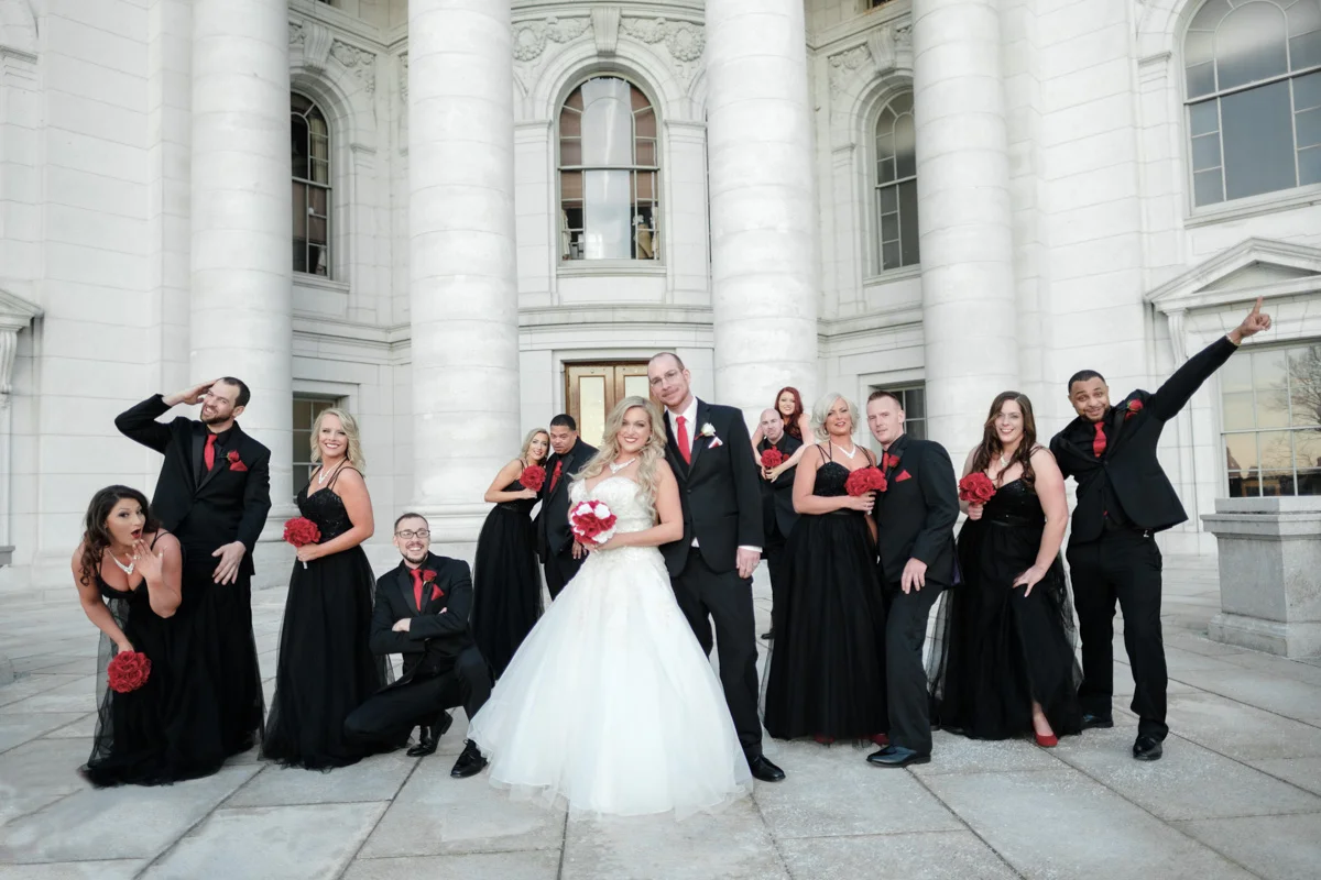Wedding party in black suits and dresses with red flowers having fun in photo with bride and groom