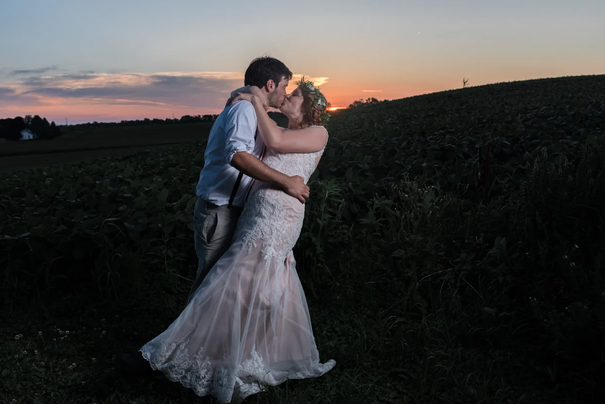 Groom dipping bride for a kiss at sunset overlooking a field at the barn at trinity peak in oconomowoc, wisconsin