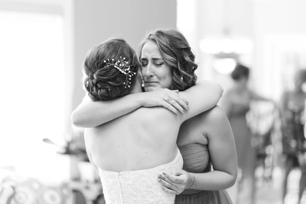 Bride and sister embrace as baby sister sees her big sister in wedding dress.