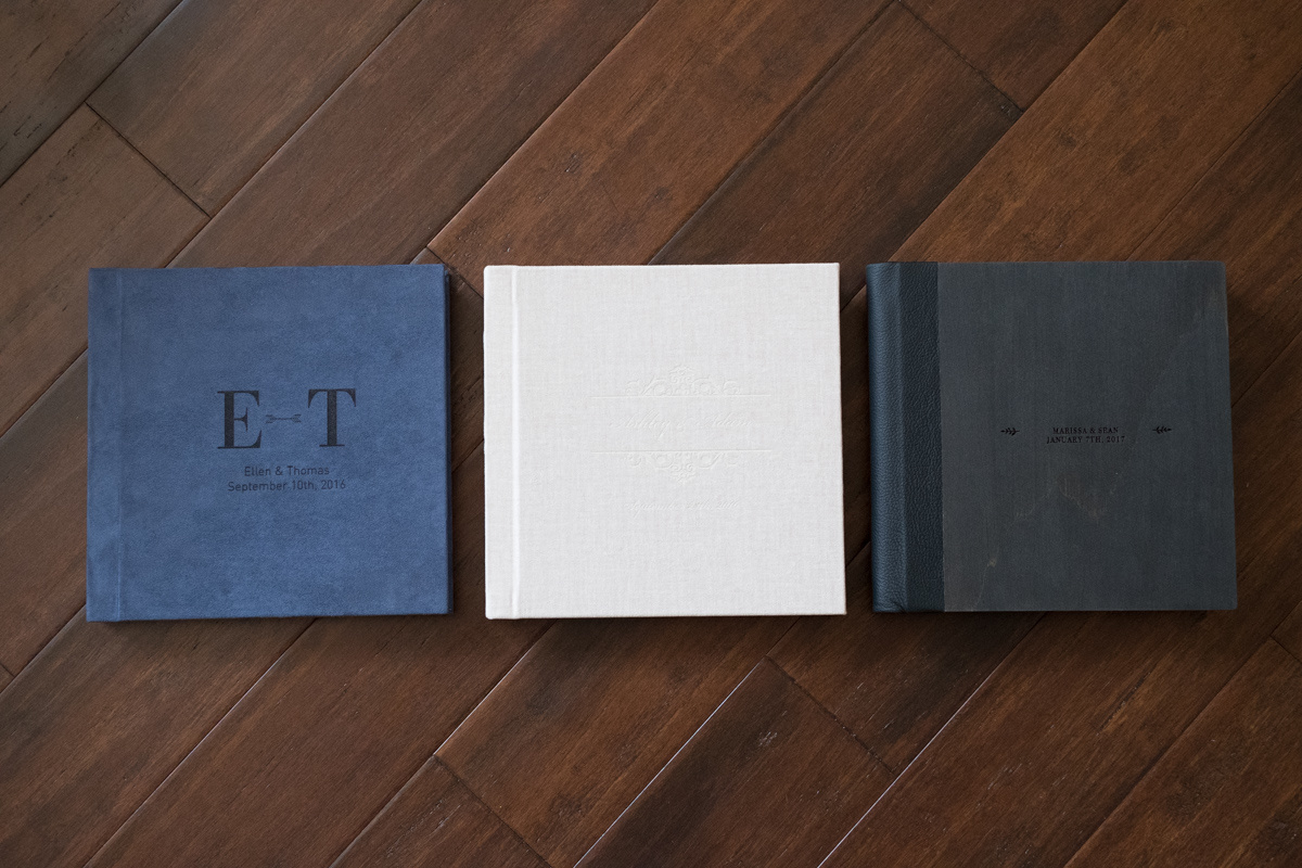  suede, linen and wood albums laying flat showing custom  engraving on each cover 