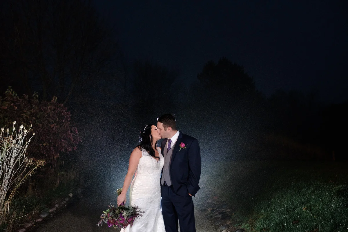 Lake Geneva Resort wedding with couple kissing after dark backlit with rain drops falling around them