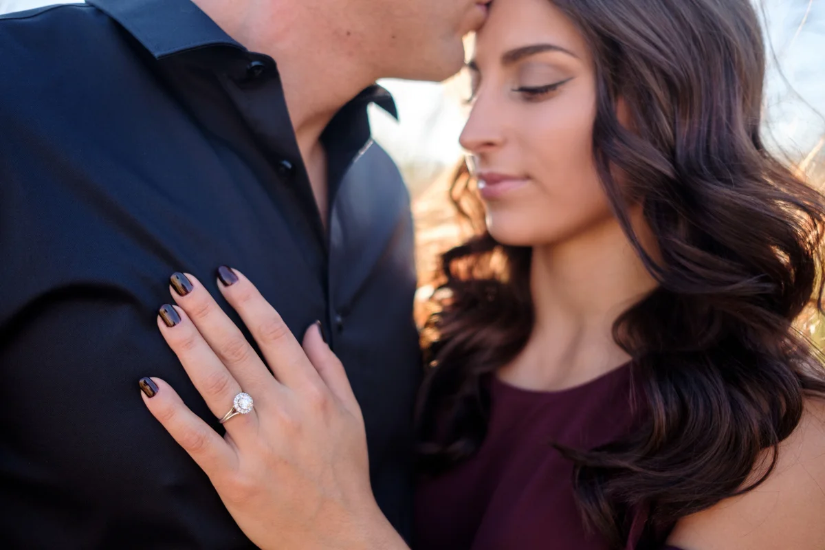 groom kissing her head with engagement ring focus resting on his chest.