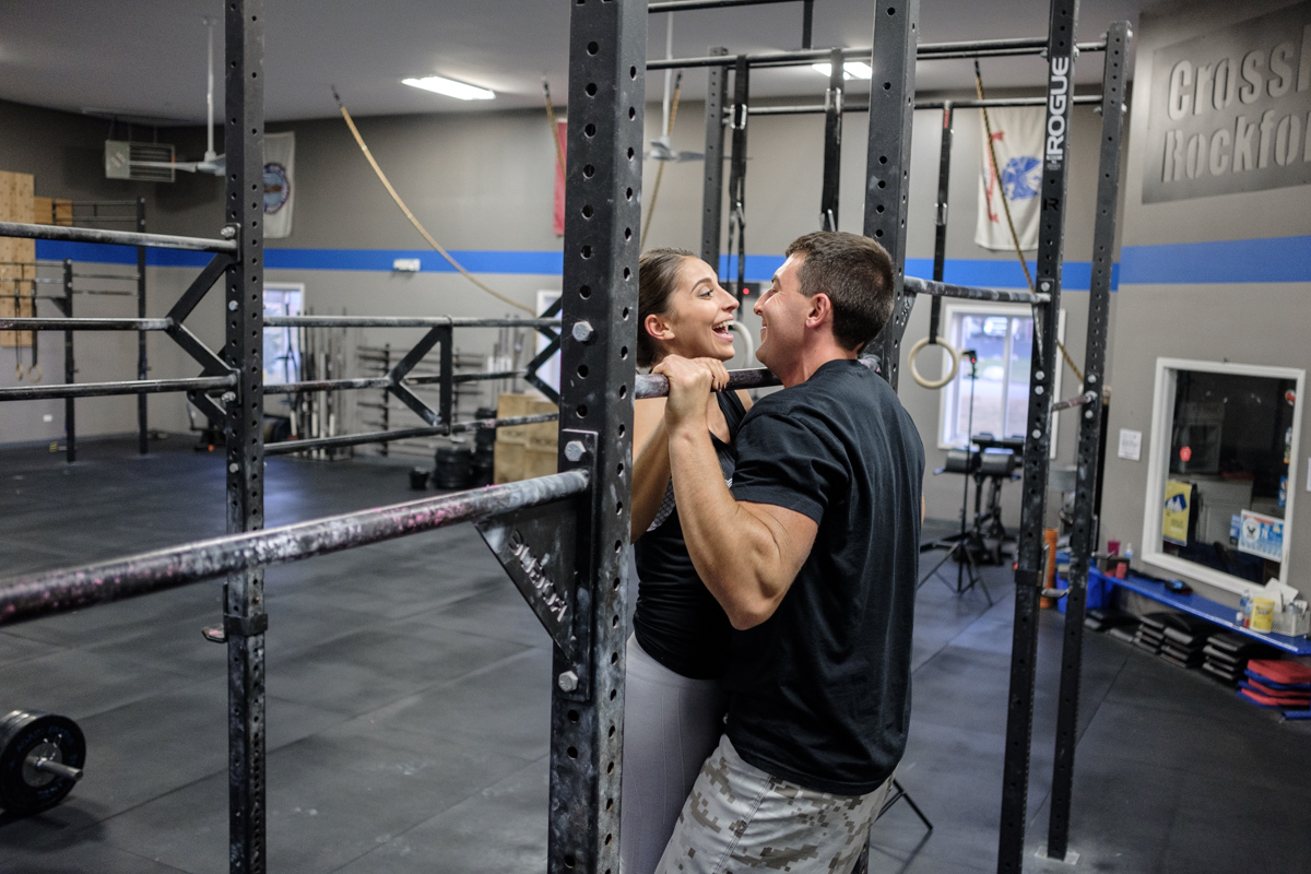 Couple kissing while doing a pull up at Crossfit Rockford during their engagement session