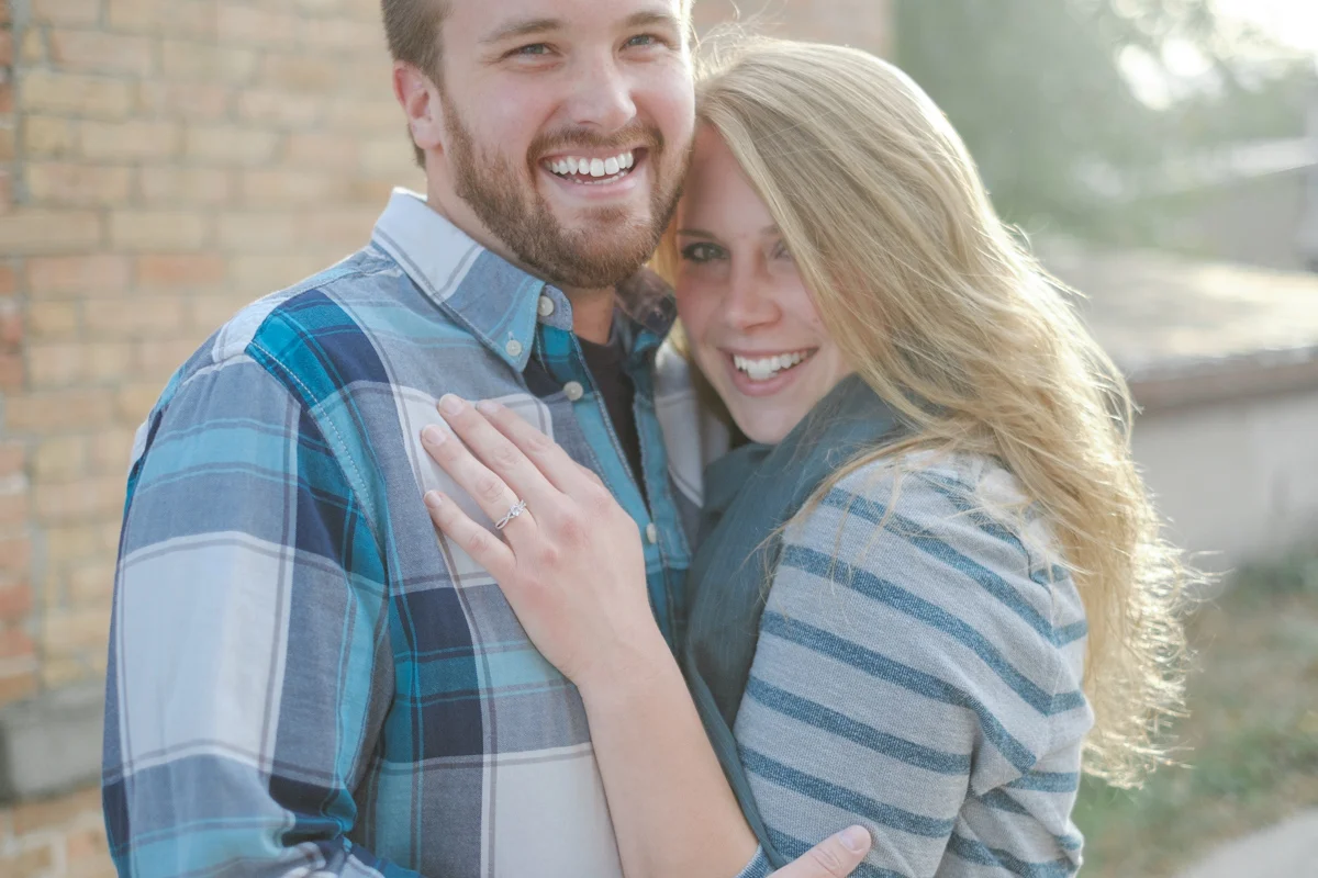 Fall engagement portrait of couple embracing in front of antique limestone building with sun setting behind them in downtown Rockton, Illinois