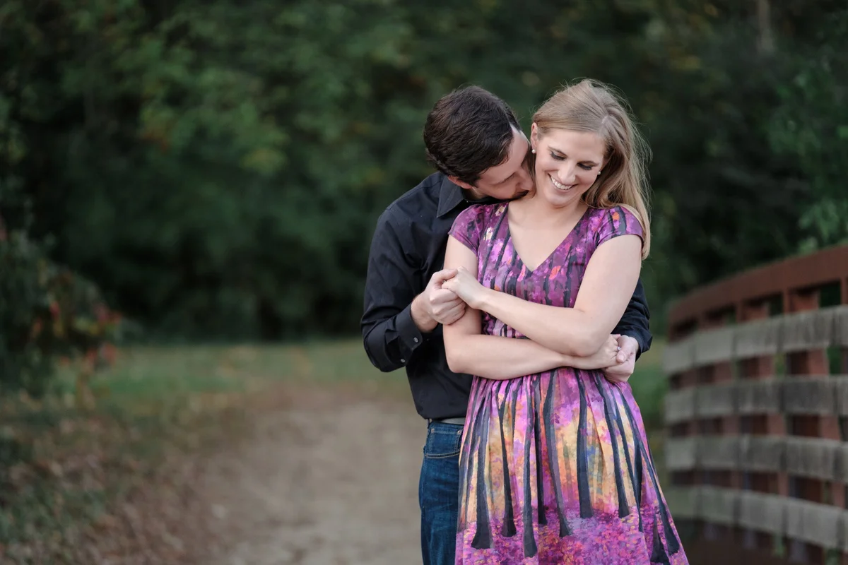 man kissing woman’s neck on bridge during engagement session at rock cut state park