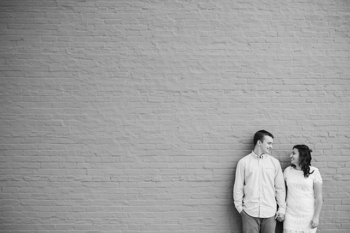 Engagement portrait of couple holding hands standing next to each other in front of painted brick wall in downtown rockton illinois