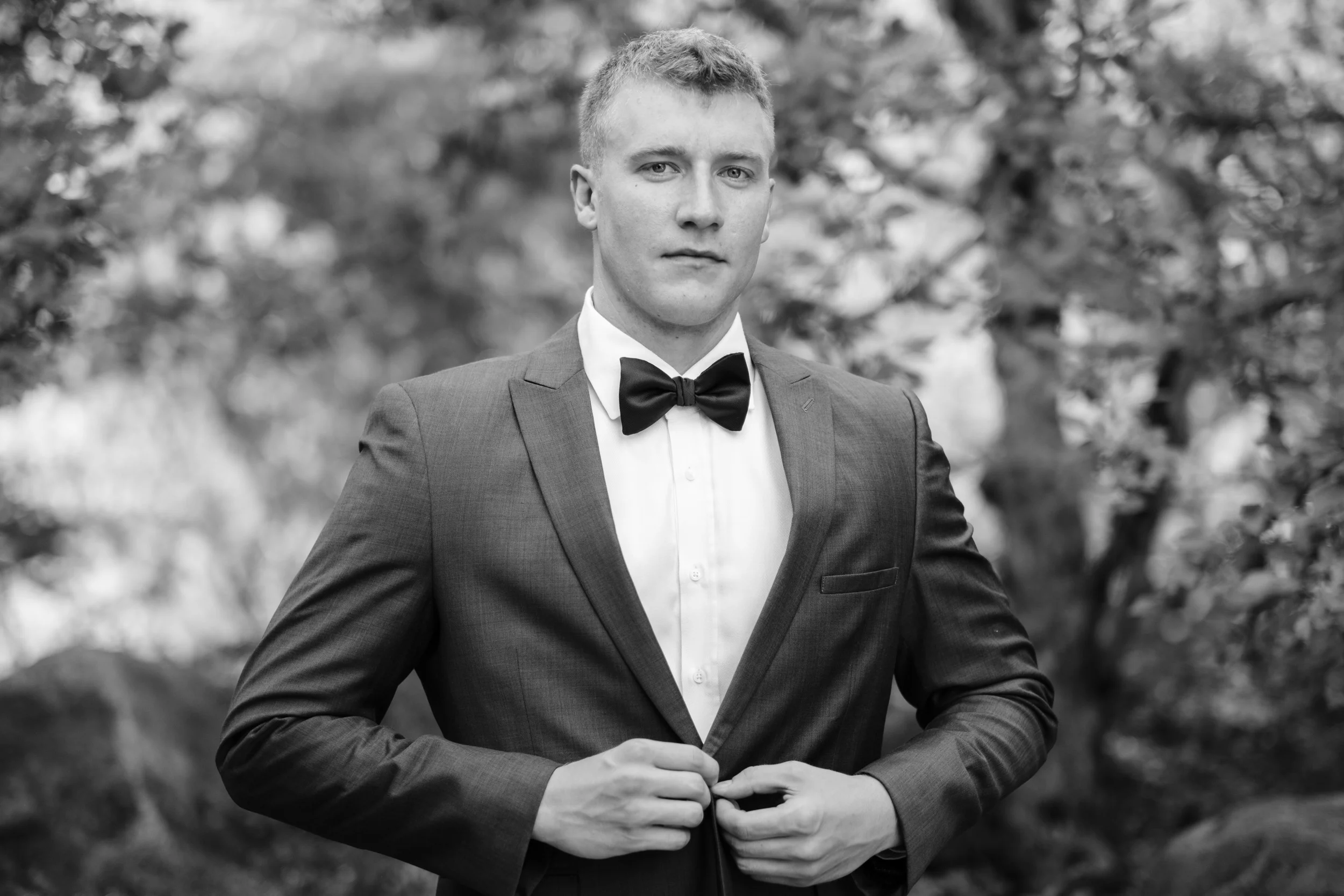 Black and white of groom buttoning his suit coat before his wedding at Anderson Japanese Gardens in Rockford, Illinois