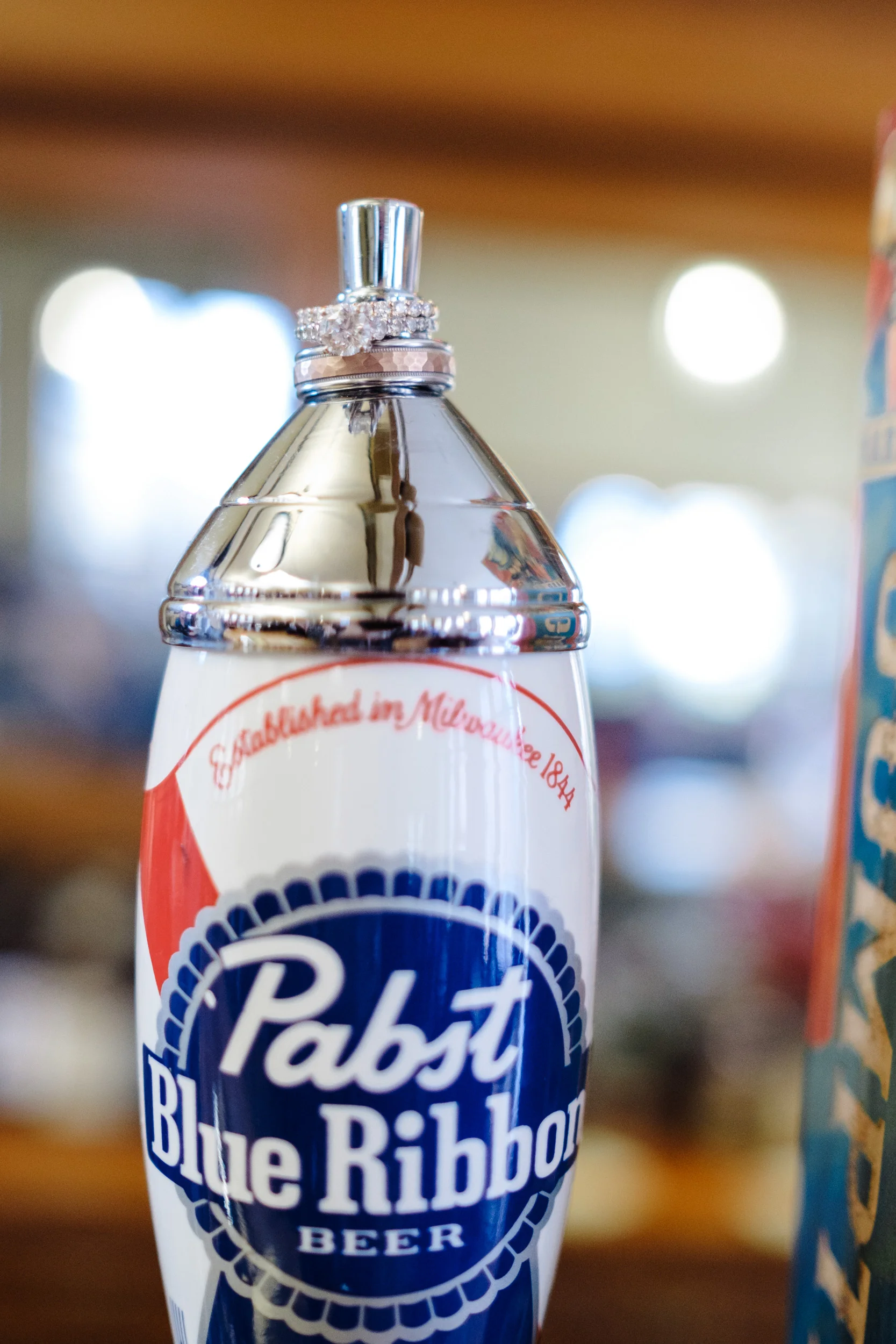 Detail ring photo of rose gold rings on pabst blue ribbon beer tap handle.