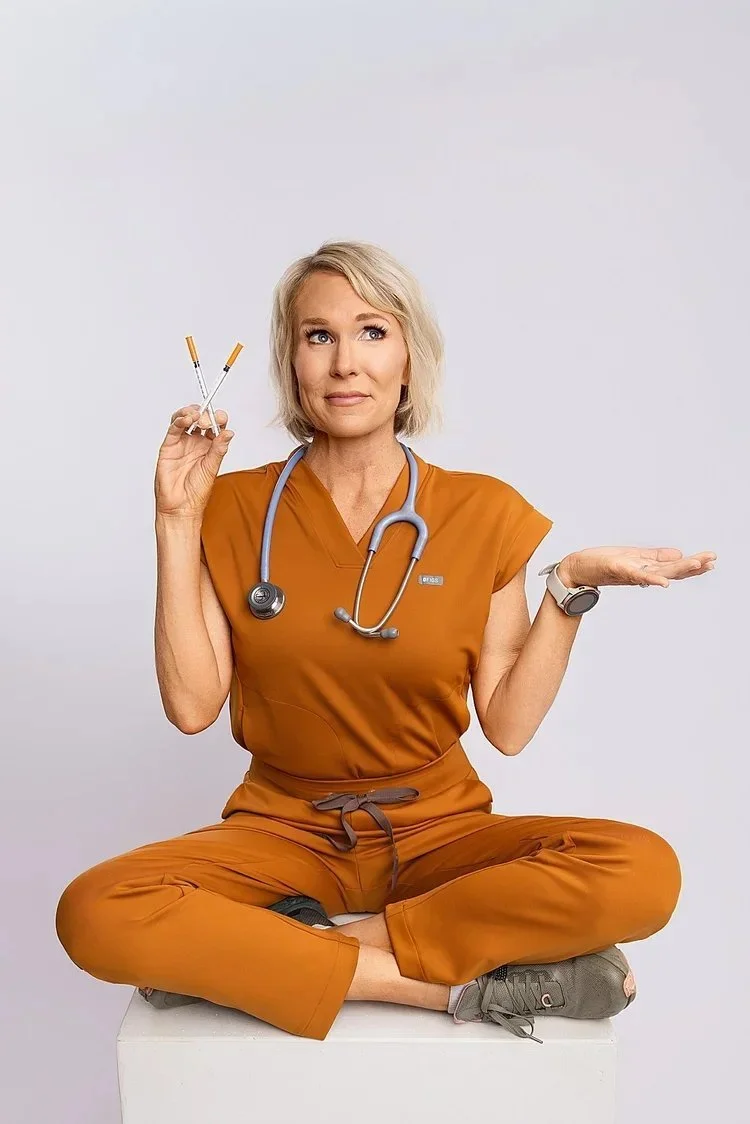 A woman wanted updated headshots and personal branding dressed as a healthcare professional sits cross-legged, holding two syringes in one hand, with a skeptical or contemplative expression.