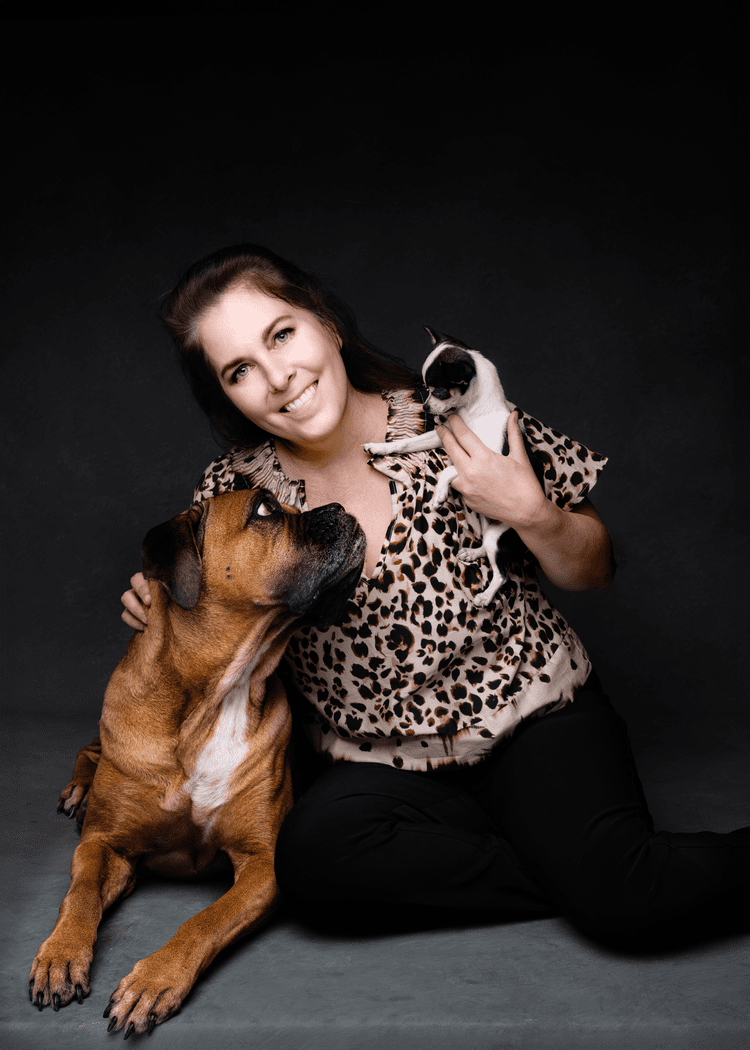 A woman sitting on the floor holding a small dog, with a large dog sitting beside her, all against a black background.