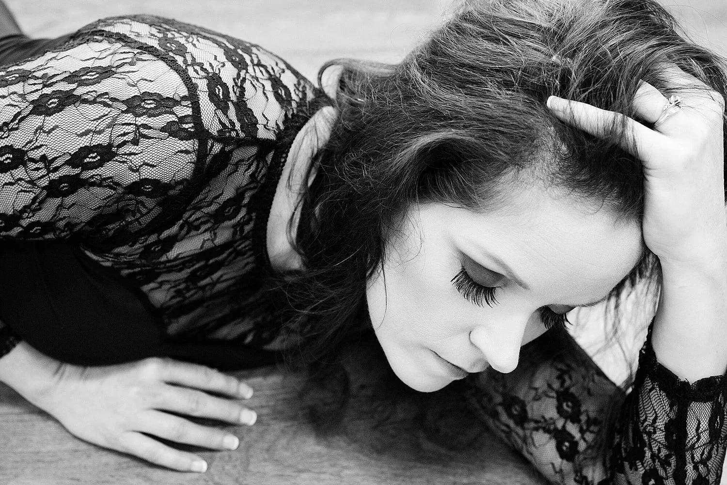 A woman in a lace top with closed eyes, holding her head with one hand, resting on a wooden surface.