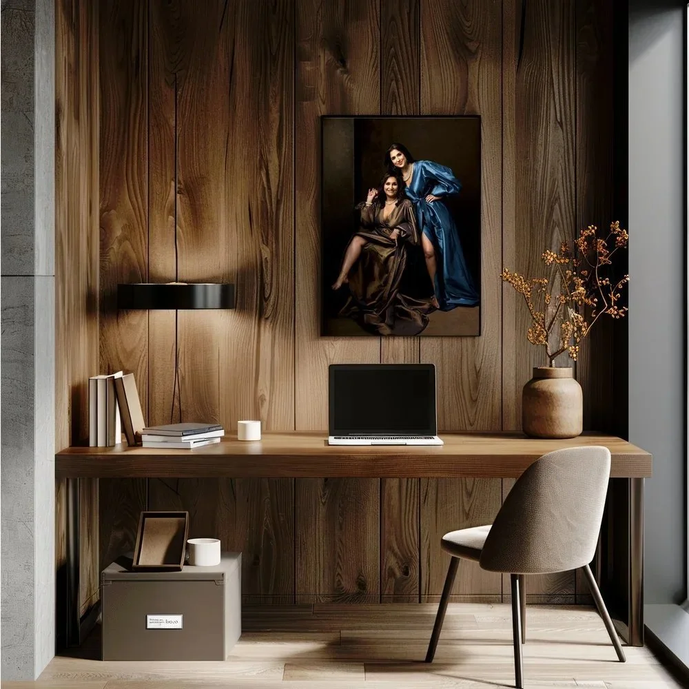 A modern home office with a wooden desk, laptop, books, a lamp, a framed photo, a large vase with branches, and a portrait painting on the wall.