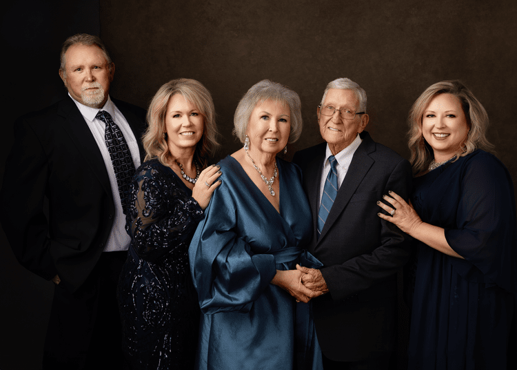 Family portrait of five adults, three women and two men, dressed in formal attire, standing together and smiling.