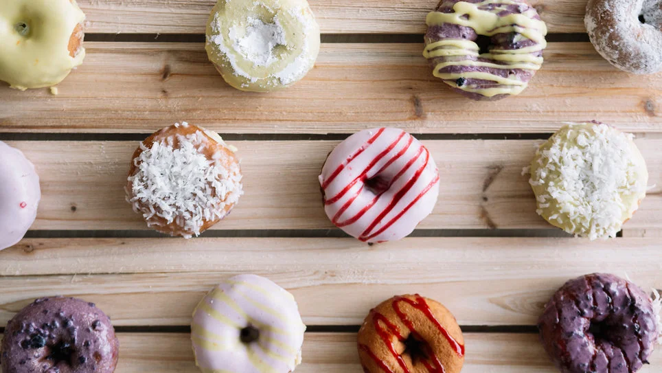 Assortment of glazed donuts with colorful strips sitting on top of a wood plank table 