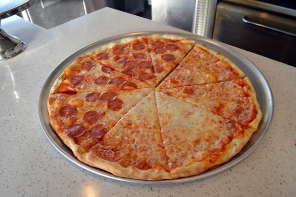 Large assorted pizza with cheese, and cheese and pepperoni pizza in a large silver pizza pan op top of a marble table