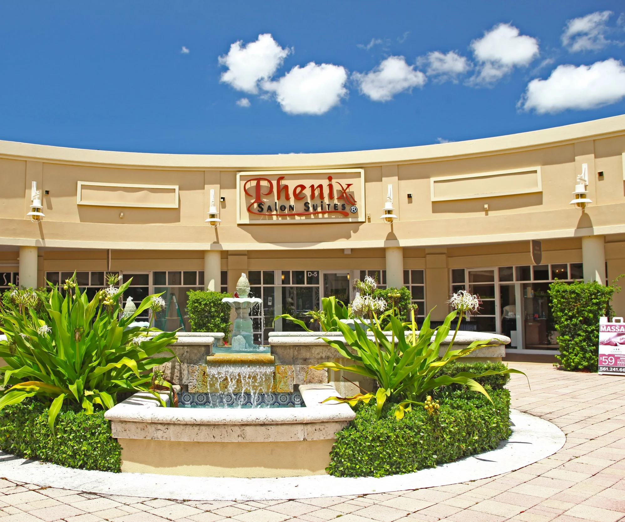 Exterior photo  Phenix Salon Suites in front of a courtyard fountain with flowing water, and lush green bushes surround the fountain 