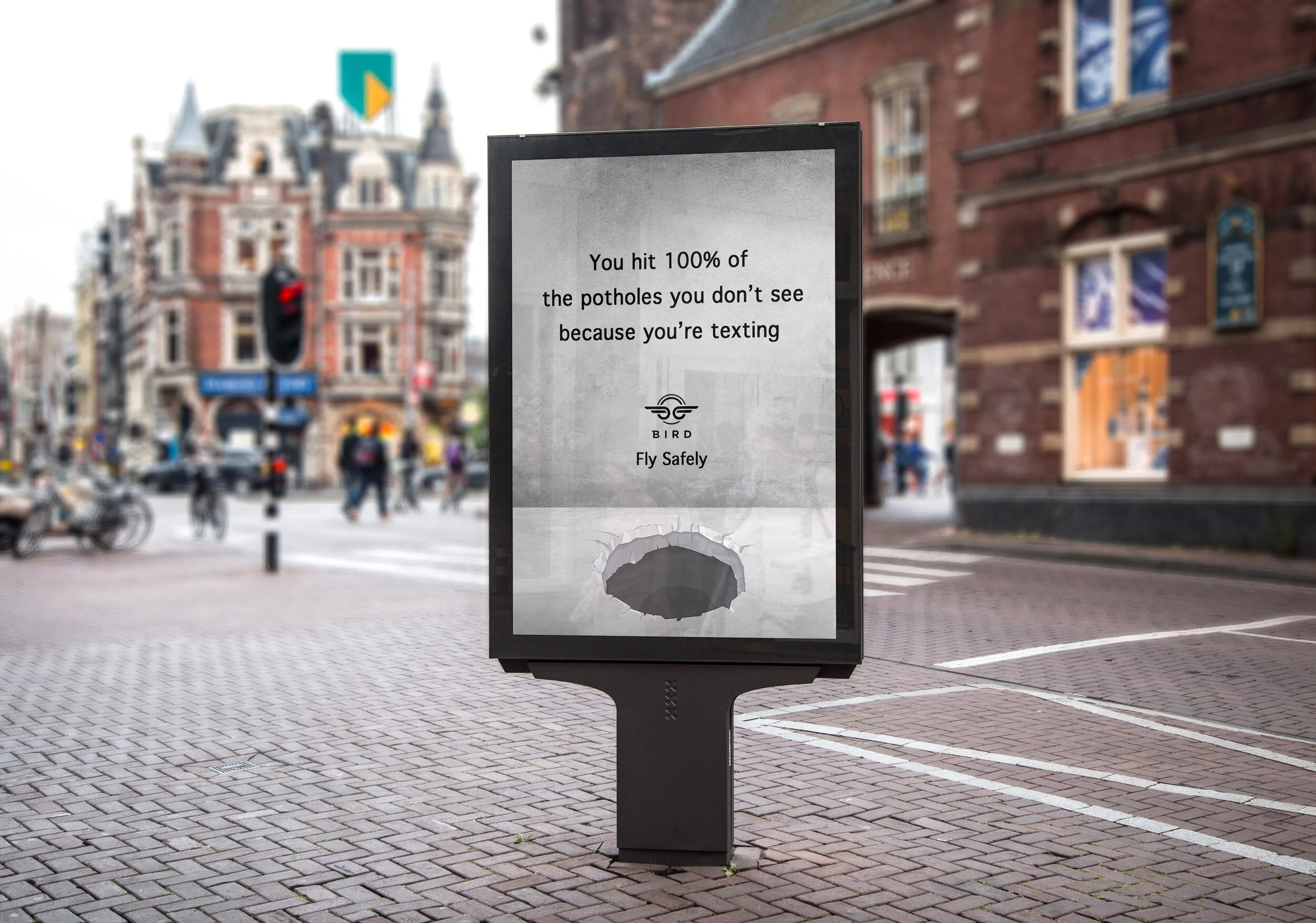 Street scene with a digital billboard showing a message about hitting potholes while texting and the Bird Rides logo, with a background of pedestrians, bicycles, and historic brick buildings.