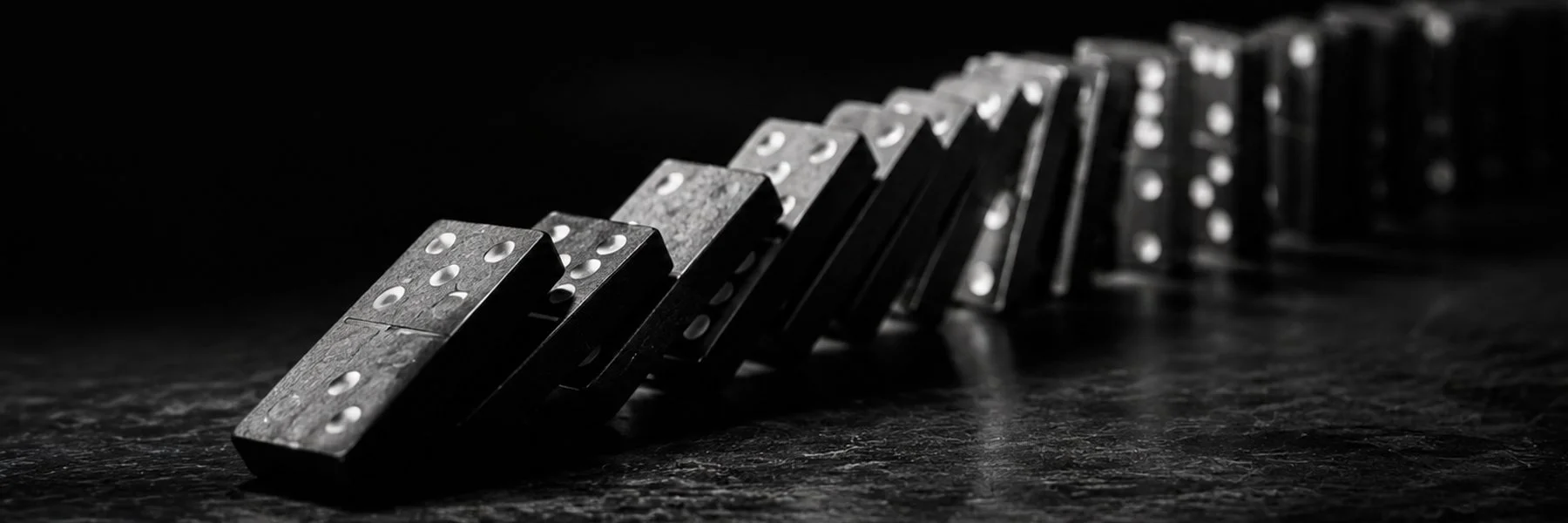 A black and white picture of a row of black dominoes with white dots, in single file, falling backward.