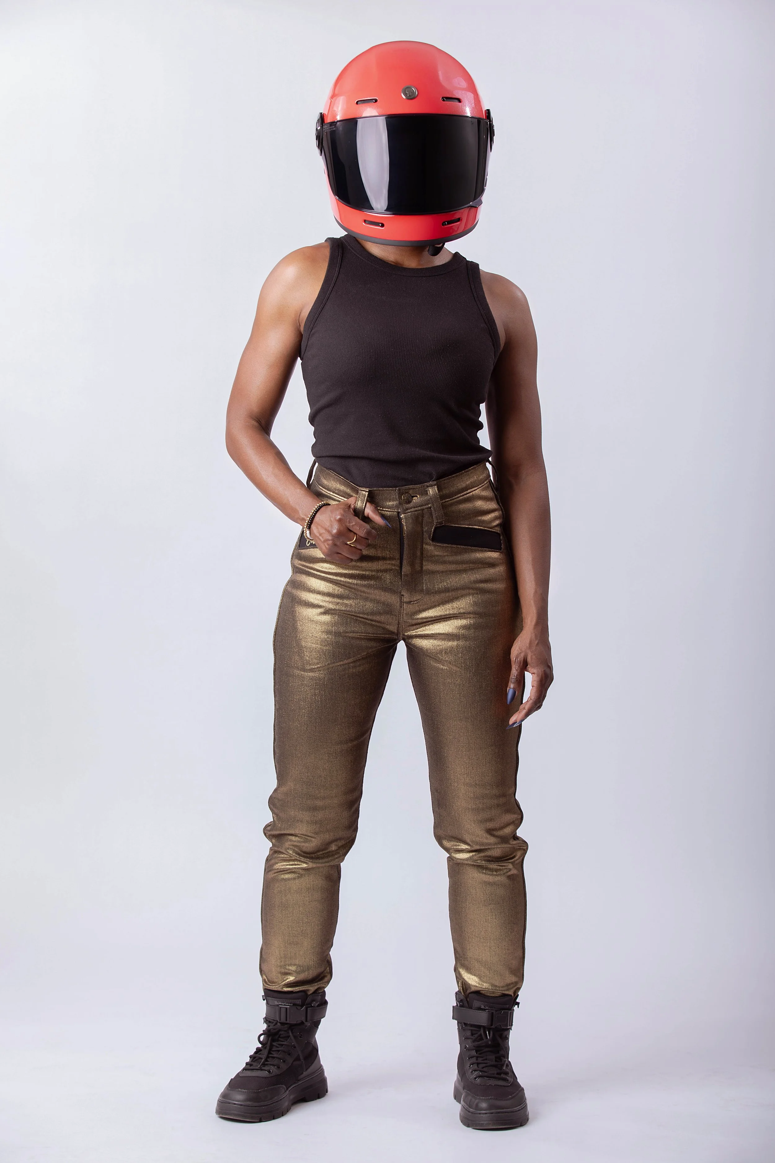 Model wearing metallic gold moto pants and black tank with red helmet, front view showing fit and styling