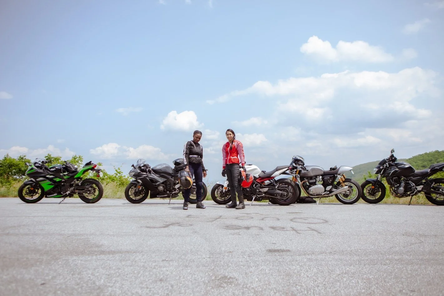 two women standing in front of motorcycles in the mountains