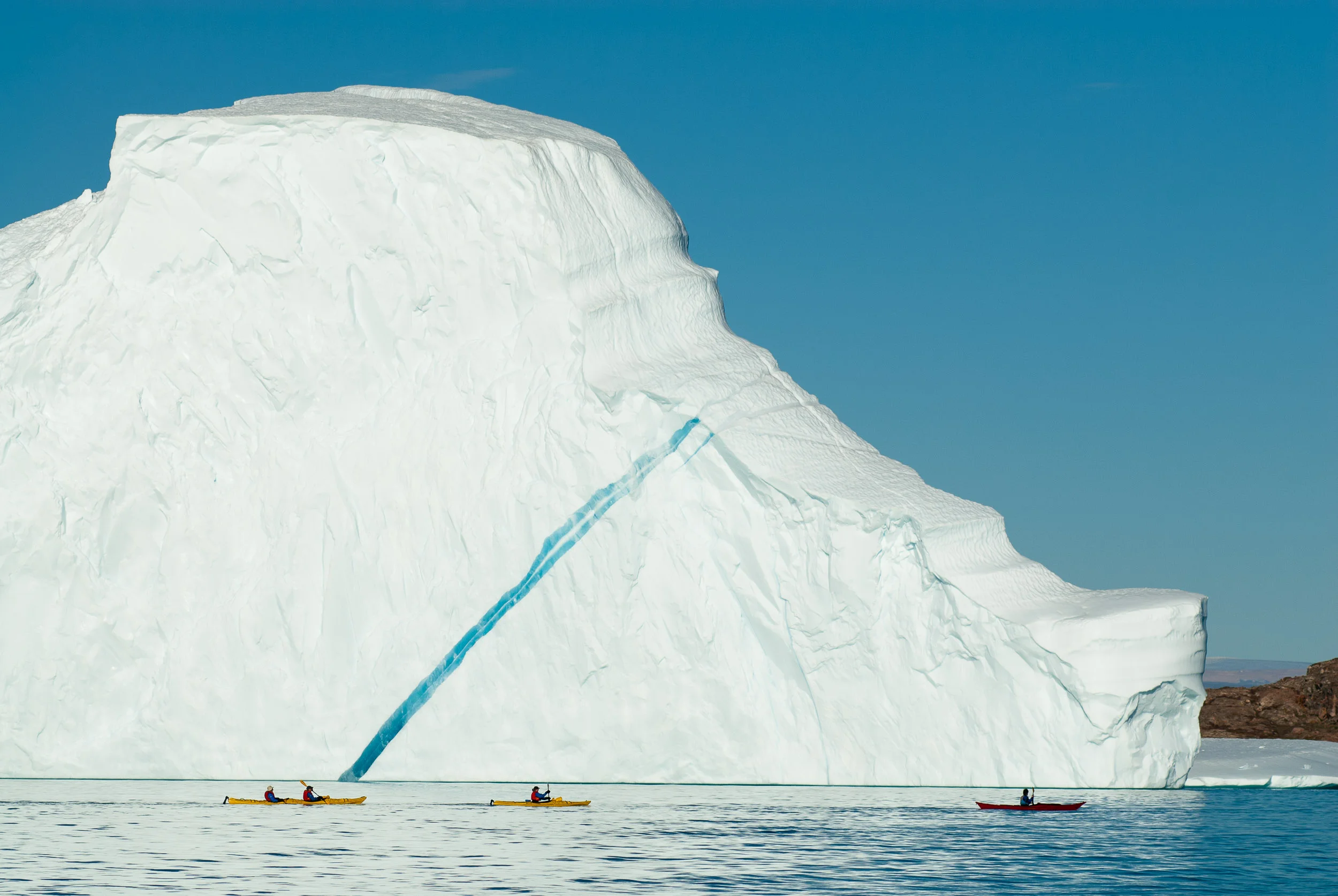 Sea kayaking Guide Solan Jenkins - in red kayak - guiding clients, east coast of Greenland. © www.thomaspickard.com