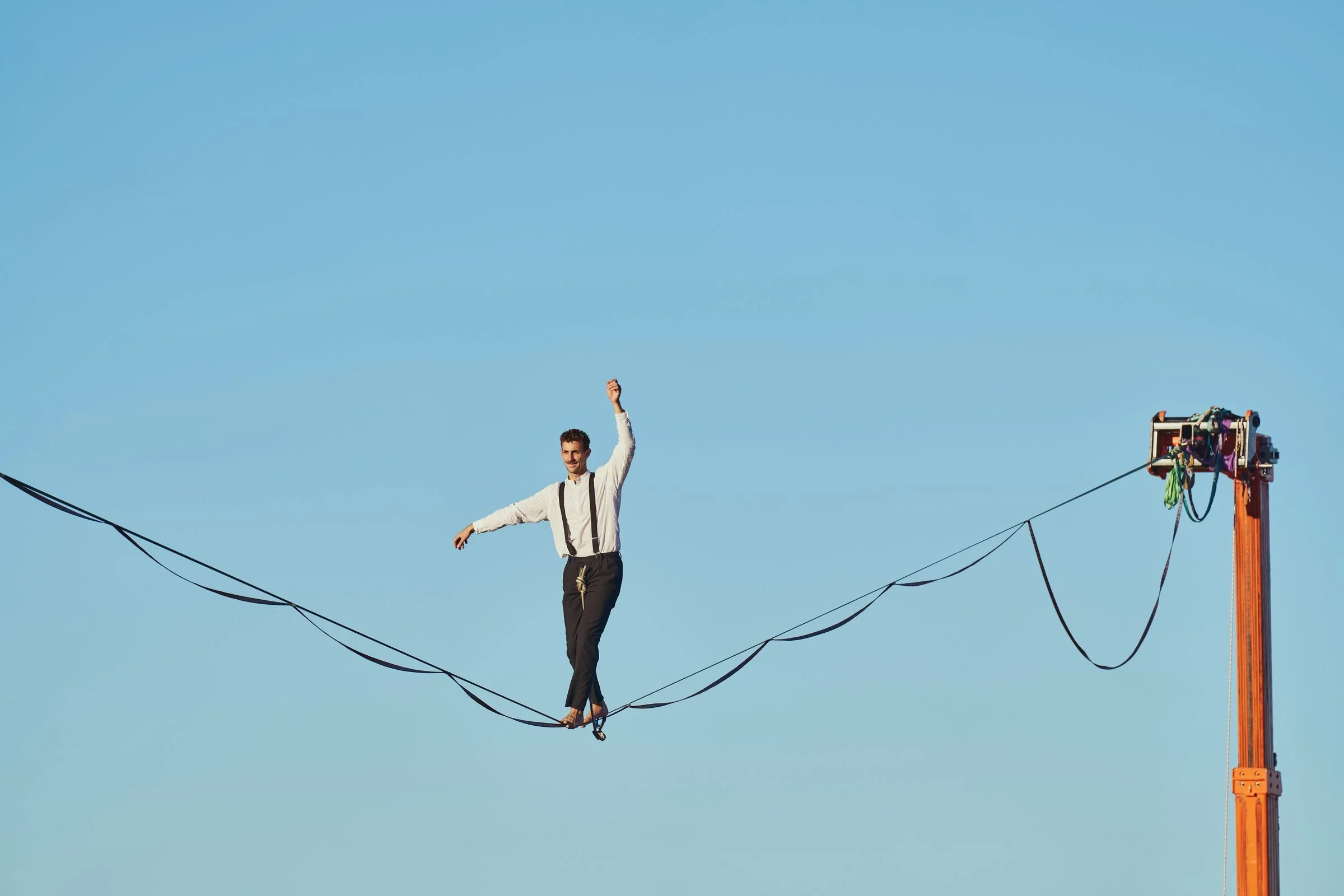 Artiste de highline en chemise blanche et bretelles, bras levé, lors du spectacle d'anniversaire d'entreprise de DIXI Polytool