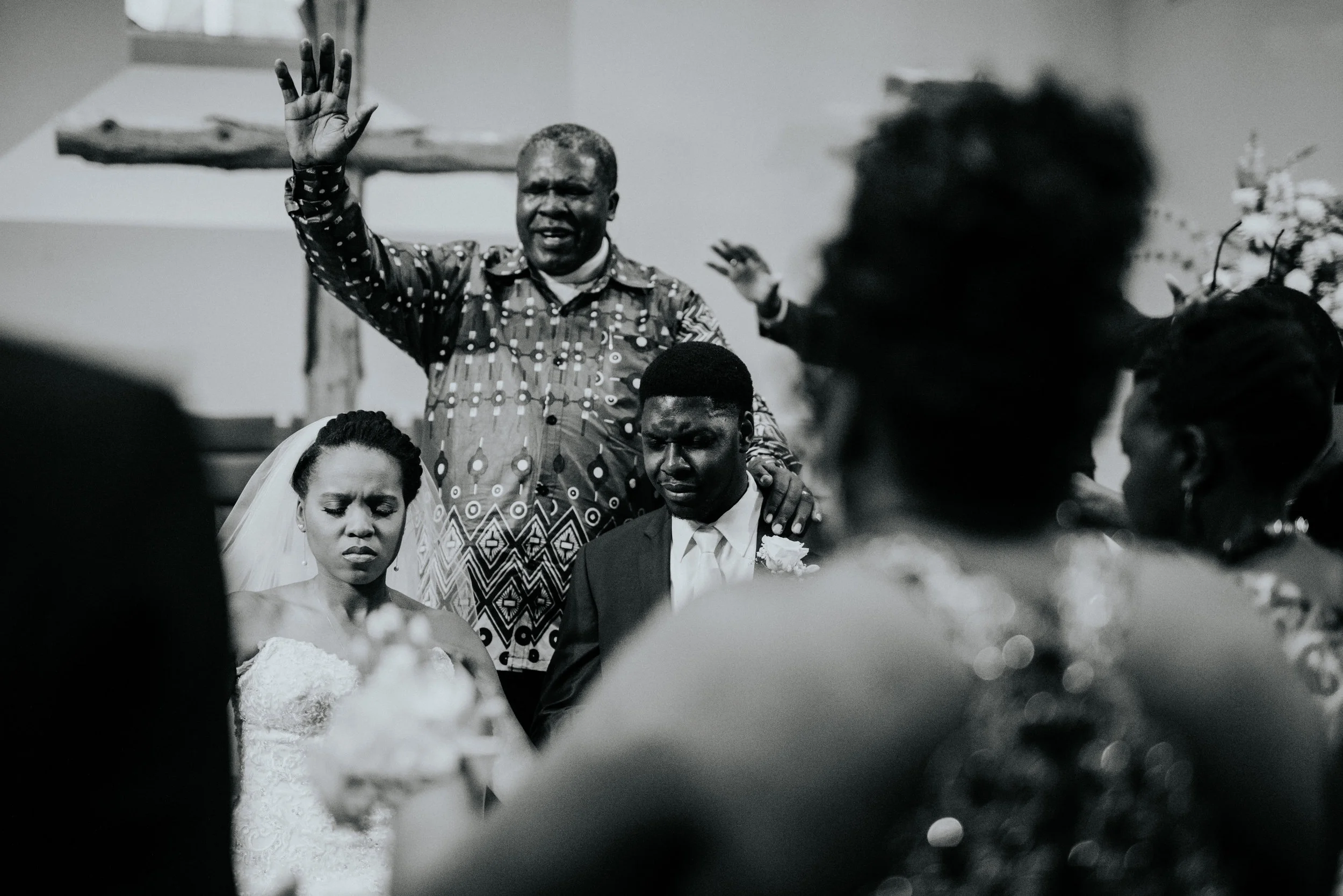 Reverend Medad praying over Joel and Jalissa with their family gathered around. Their friends reached out hands from the pews as well.