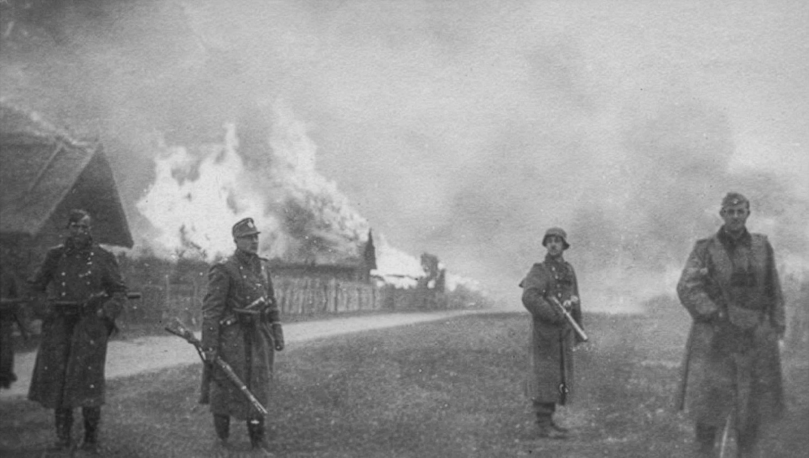 Armed German Ordnungspolizei standing in a road as wooden houses burn during a punitive operation in occupied Belarus, Mogilev region, October 1943.
