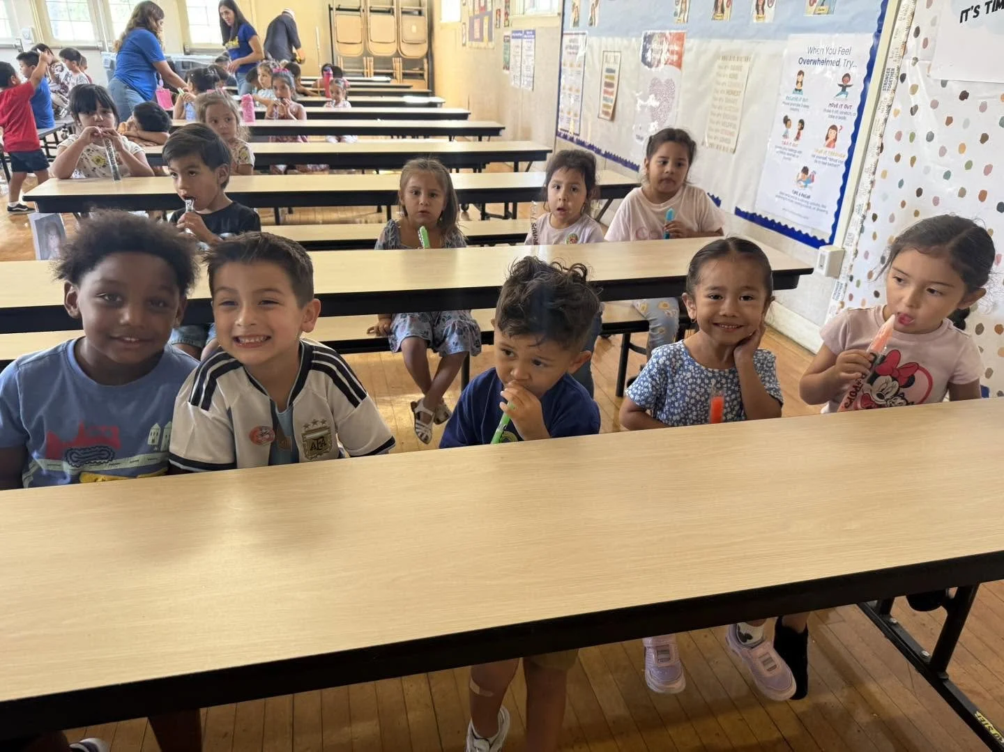 Young Condors enjoy ice pops together while seated at long cafeteria tables.