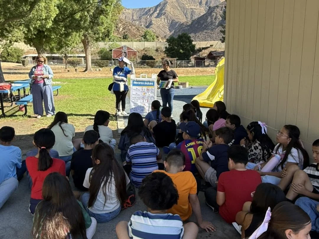 Students listen to staff explaining recess rules near the play structure.