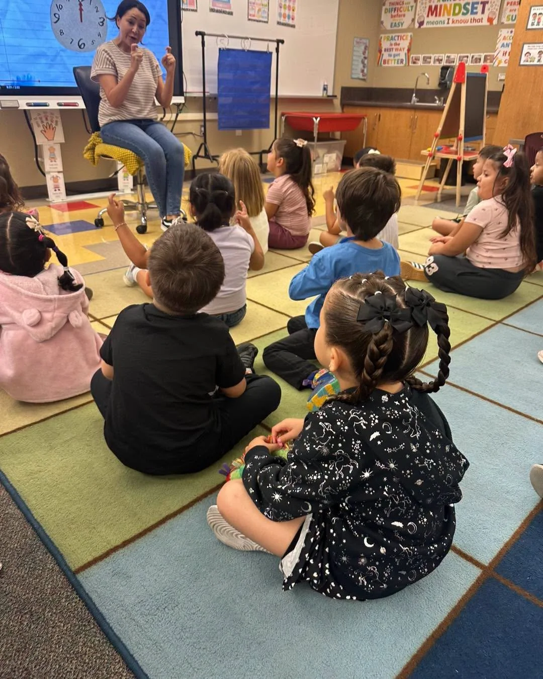 A teacher leads a lesson with students seated on the classroom rug.