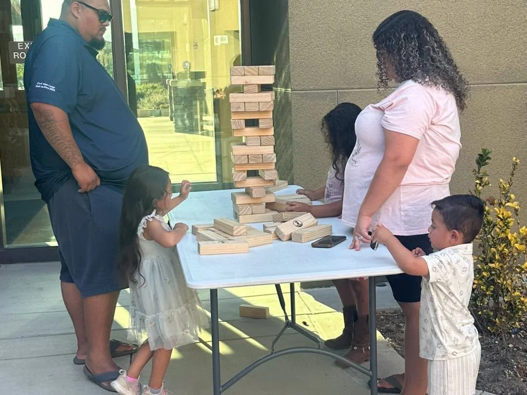 A family plays an oversized wooden block stacking game outdoors.