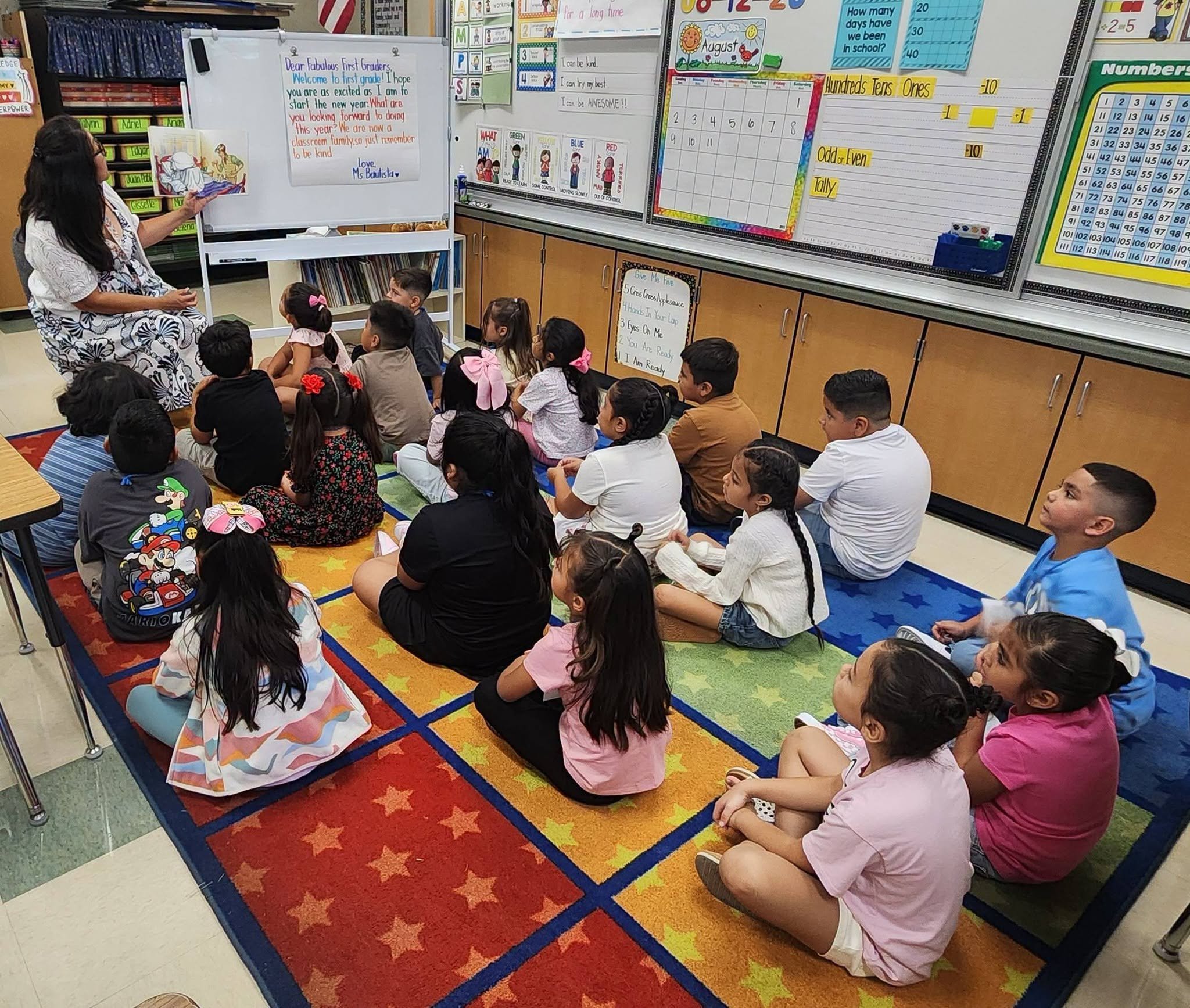 A teacher reads a picture book to students seated on the classroom rug.