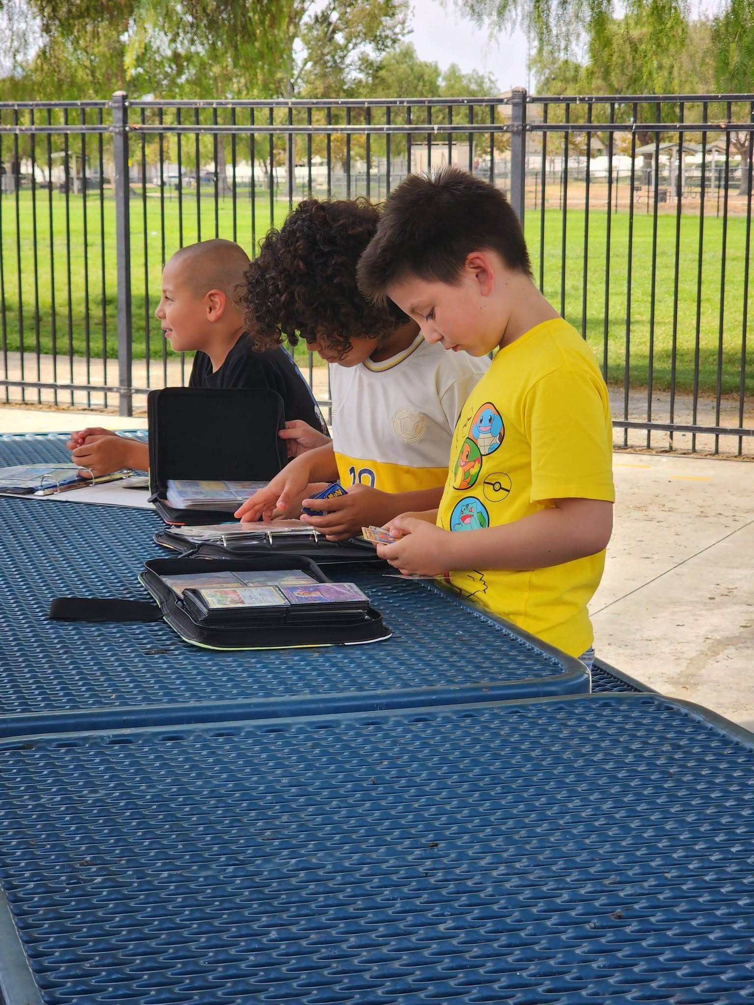 Students look through Pokémon card binders and compare cards at an outdoor picnic table.