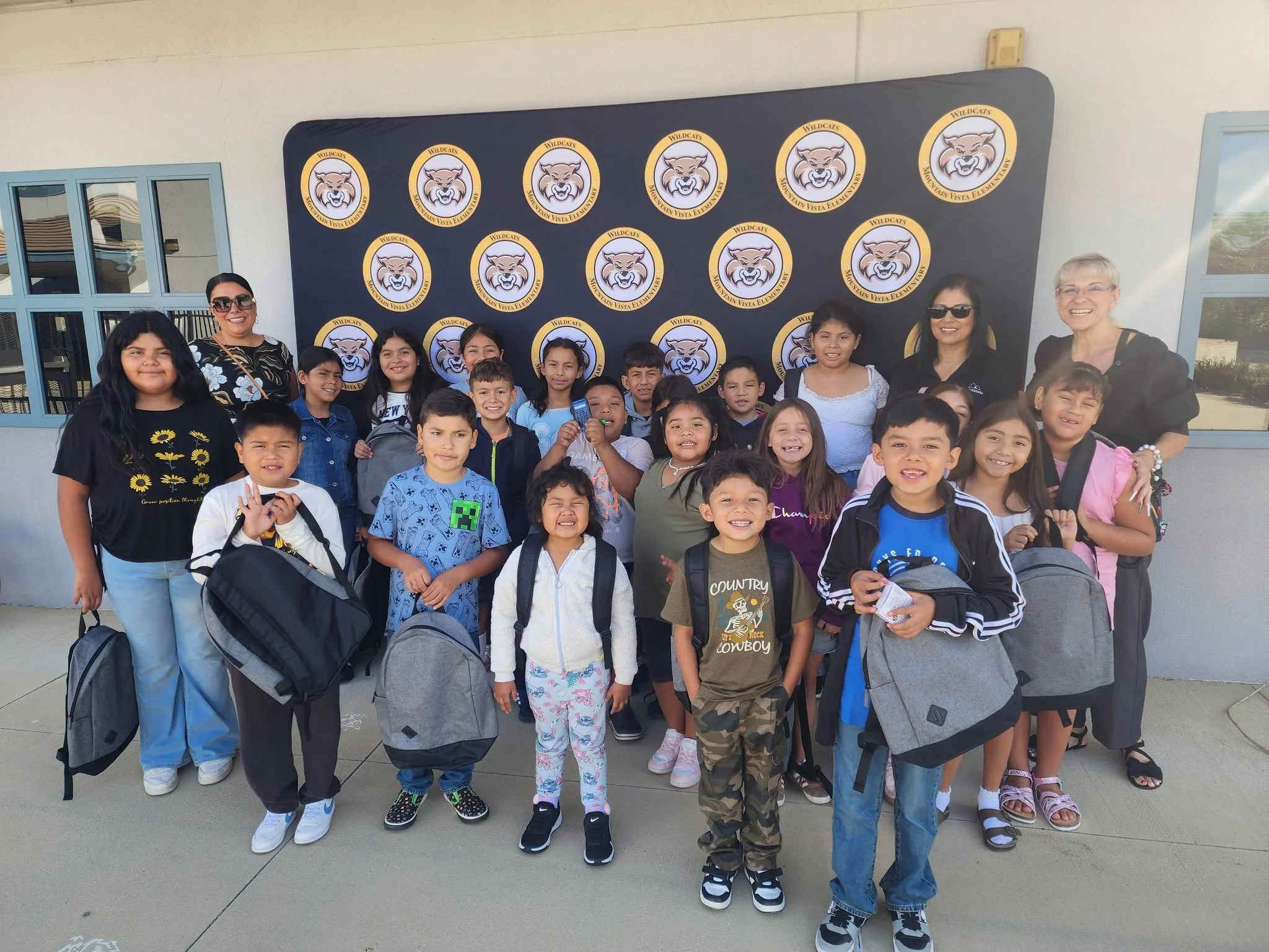 Students and adults pose with donated backpacks in front of the Wildcats banner.