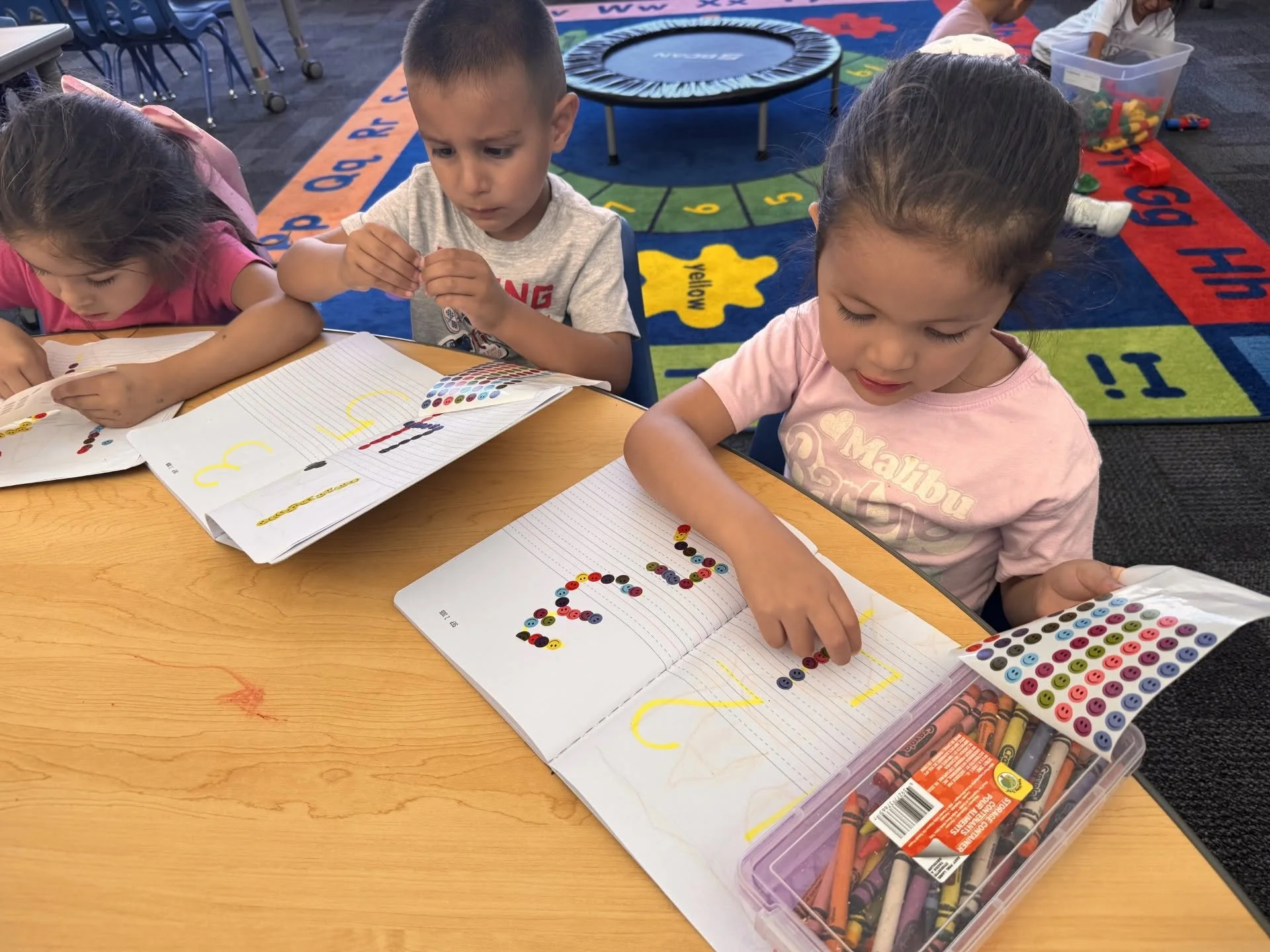 TK students use colorful stickers to form numbers in their classroom notebooks.