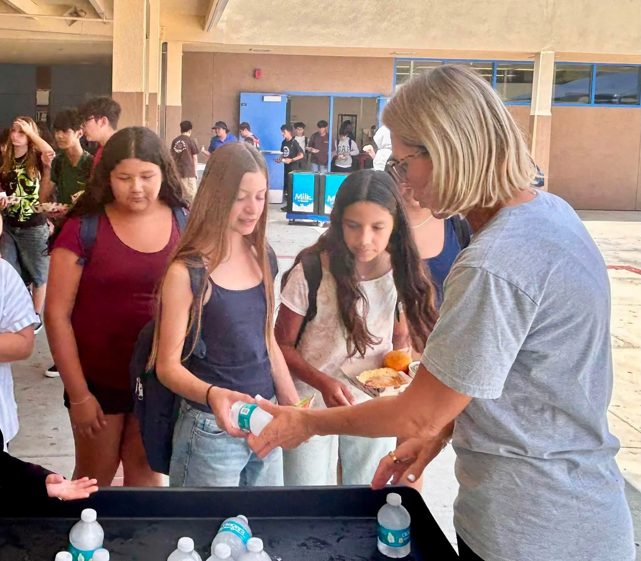 Mrs. Plugge gives a cold water bottle to a student carrying lunch.