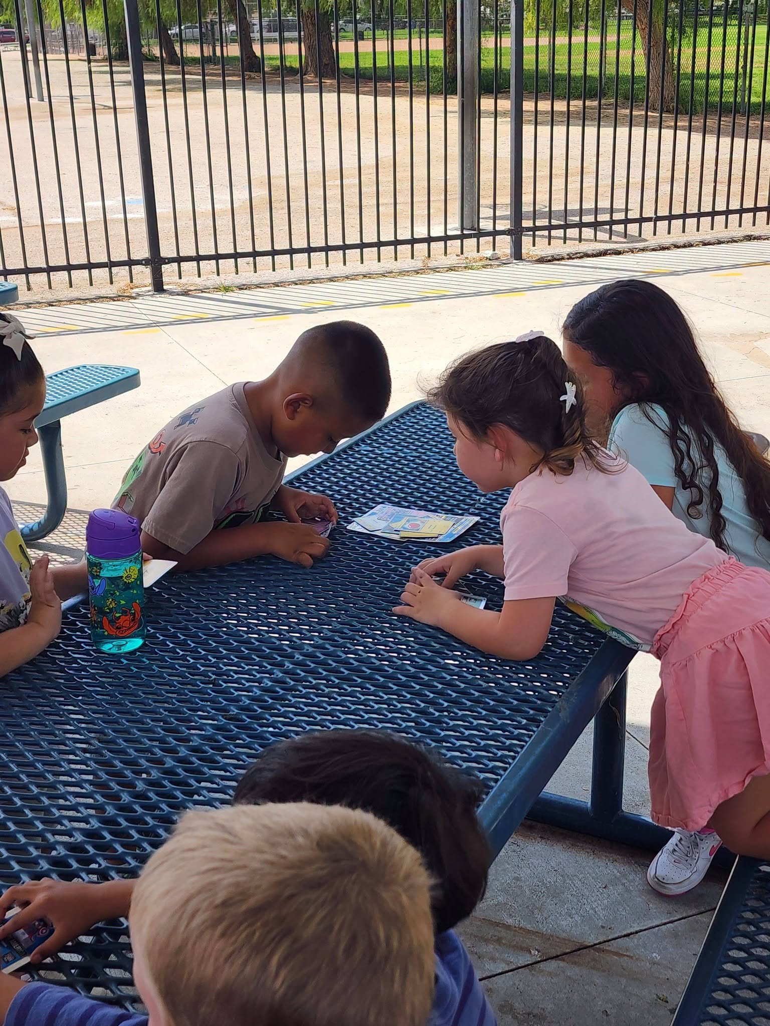 Students lean over a picnic table to examine Pokémon cards together.