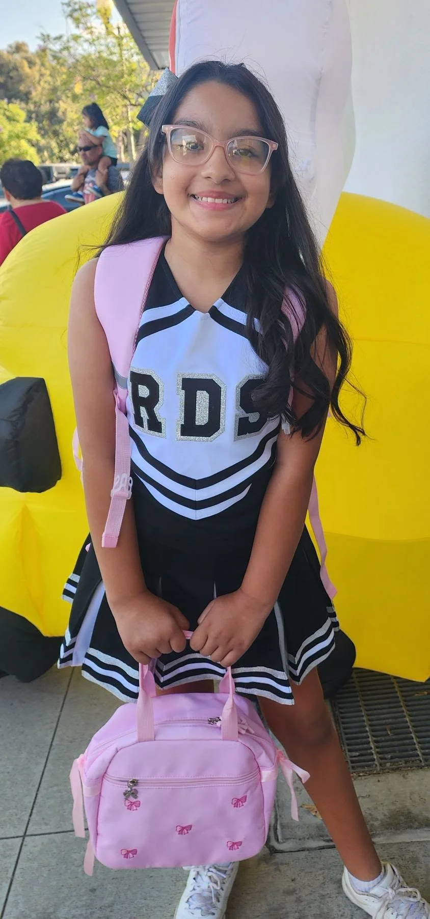 A student in a cheer uniform poses with a pink backpack and lunch bag.