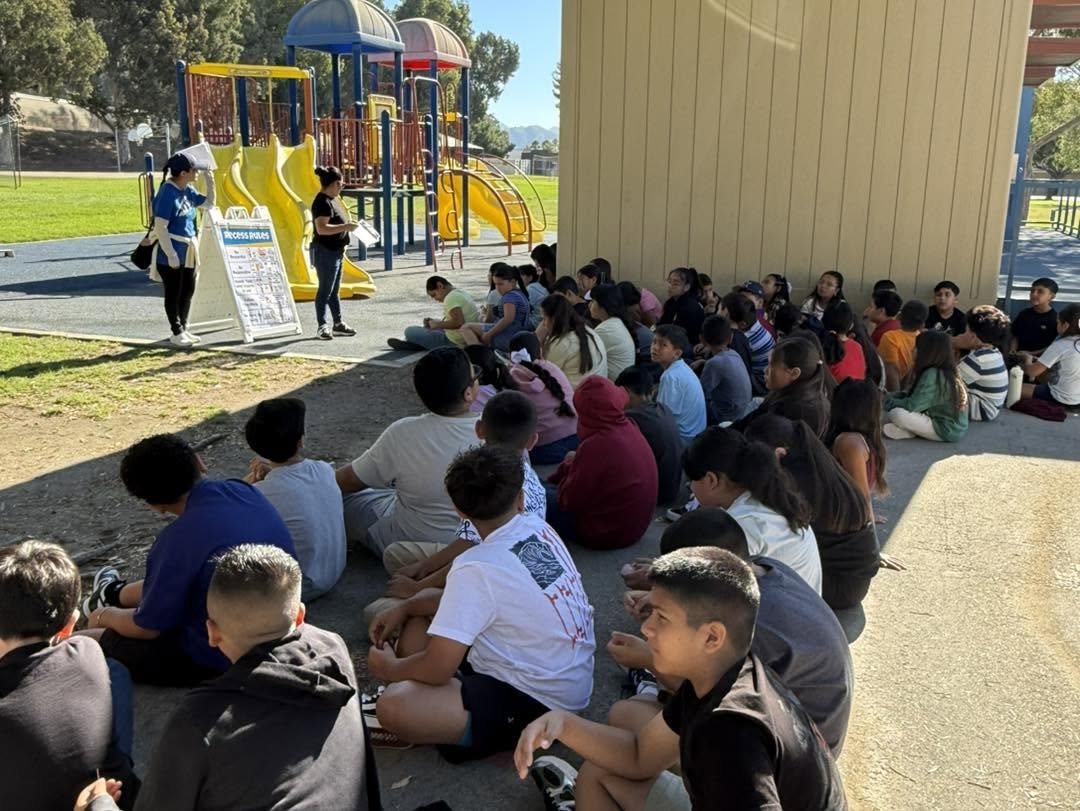 Staff explain recess rules to students seated beside the playground.