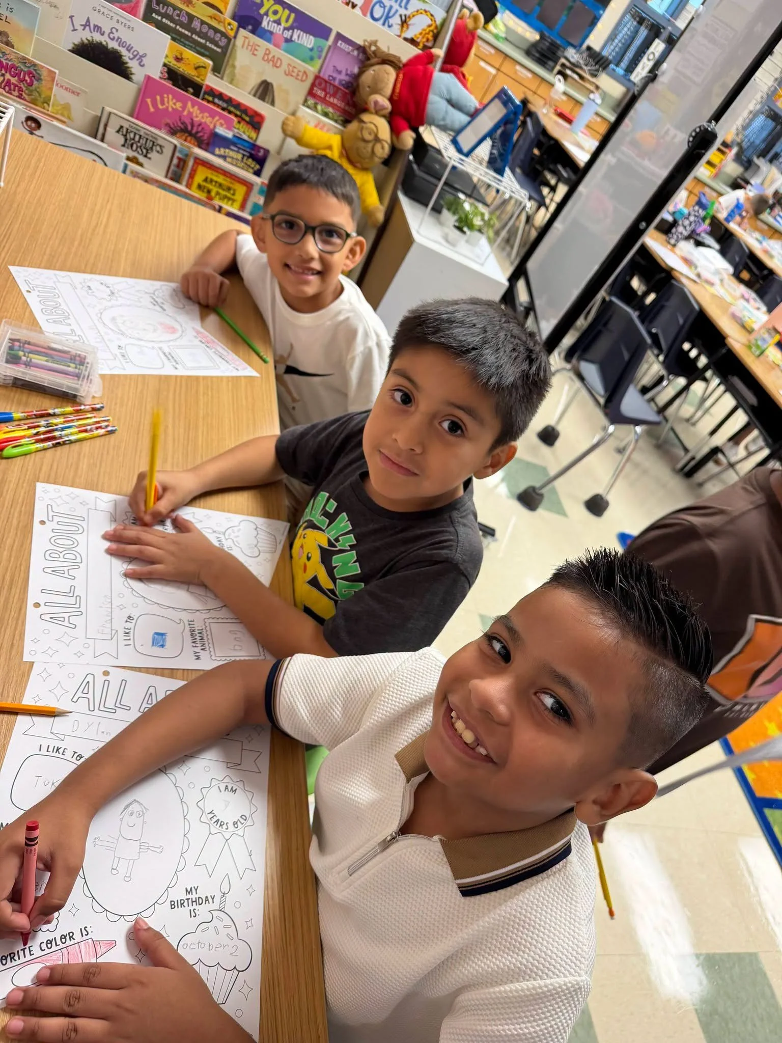Students draw and write about themselves at a classroom table.