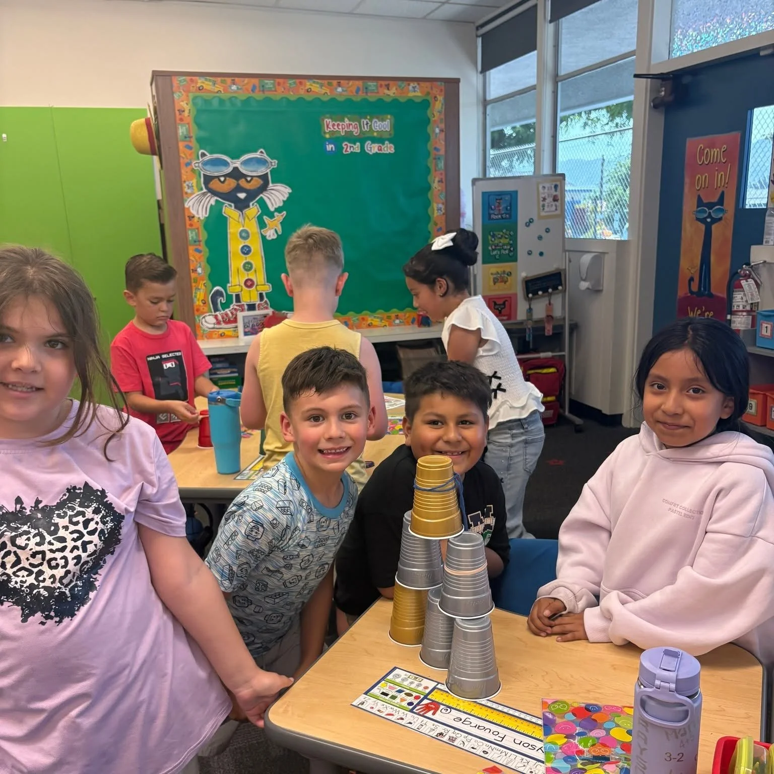 Students smile beside a tower of stacked cups in their classroom.