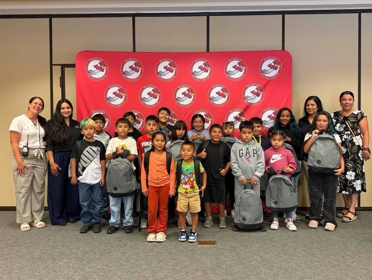 Students and adults display donated backpacks in front of the Rio Vista banner.