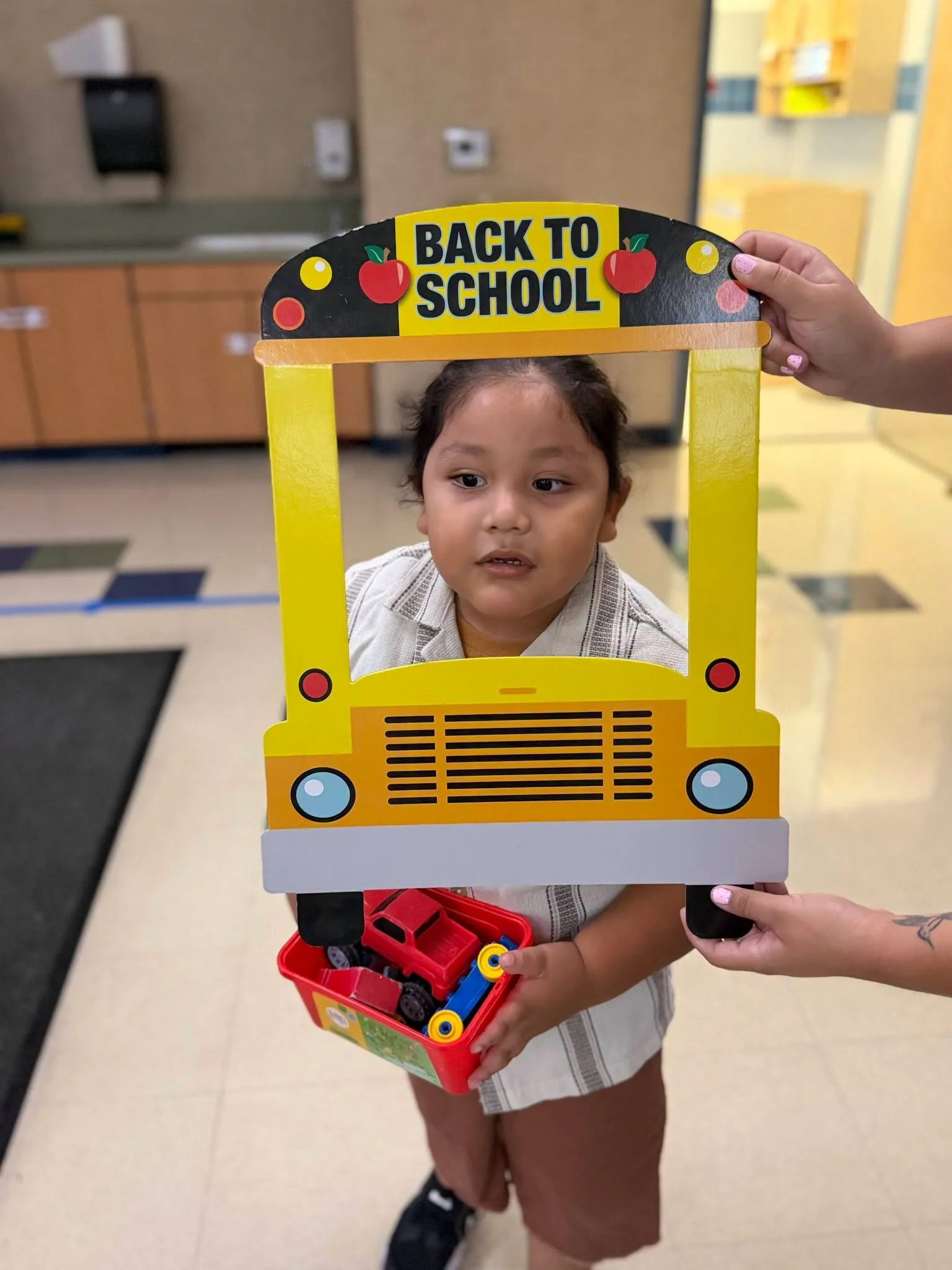A student holding a toy vehicle poses through the school-bus frame.