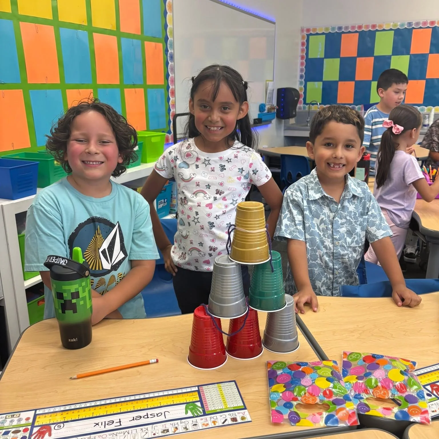 Three students show a colorful cup tower built together on the first day.