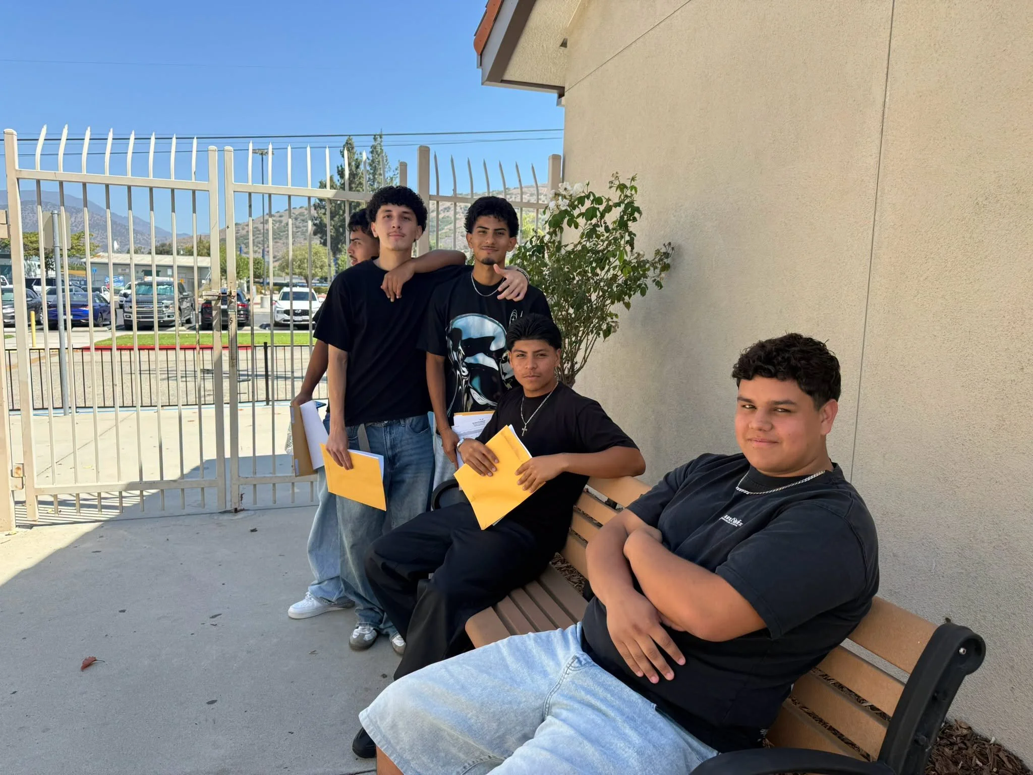 Students sit and stand beside a campus bench with registration papers at Fillmore High School.