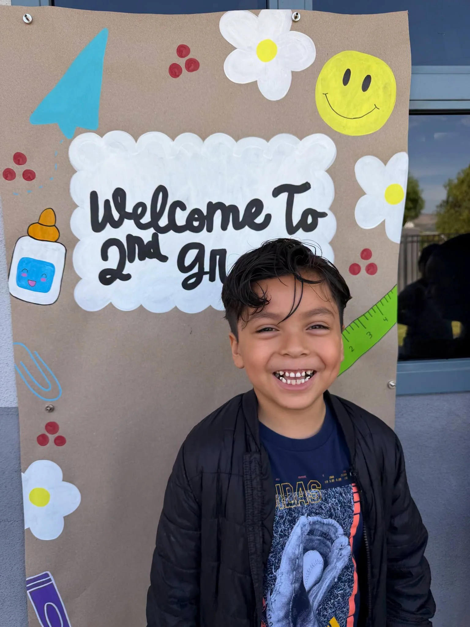 A student smiles beside a Welcome to Second Grade sign.